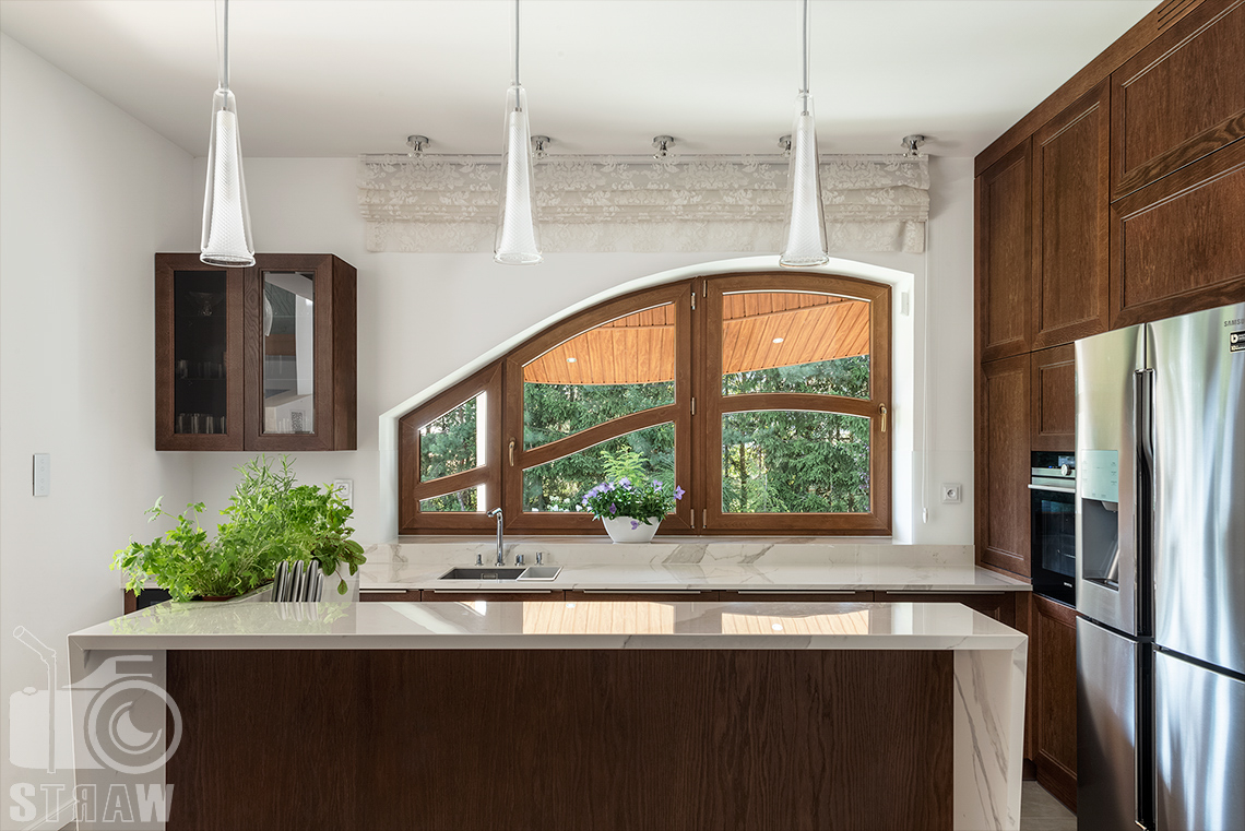 Fotografia wnętrz domu zaprojektowanego przez biuro projektowe, kuchnia, zabudowa kuchenna w drewnie, wiszące lampy i okno.