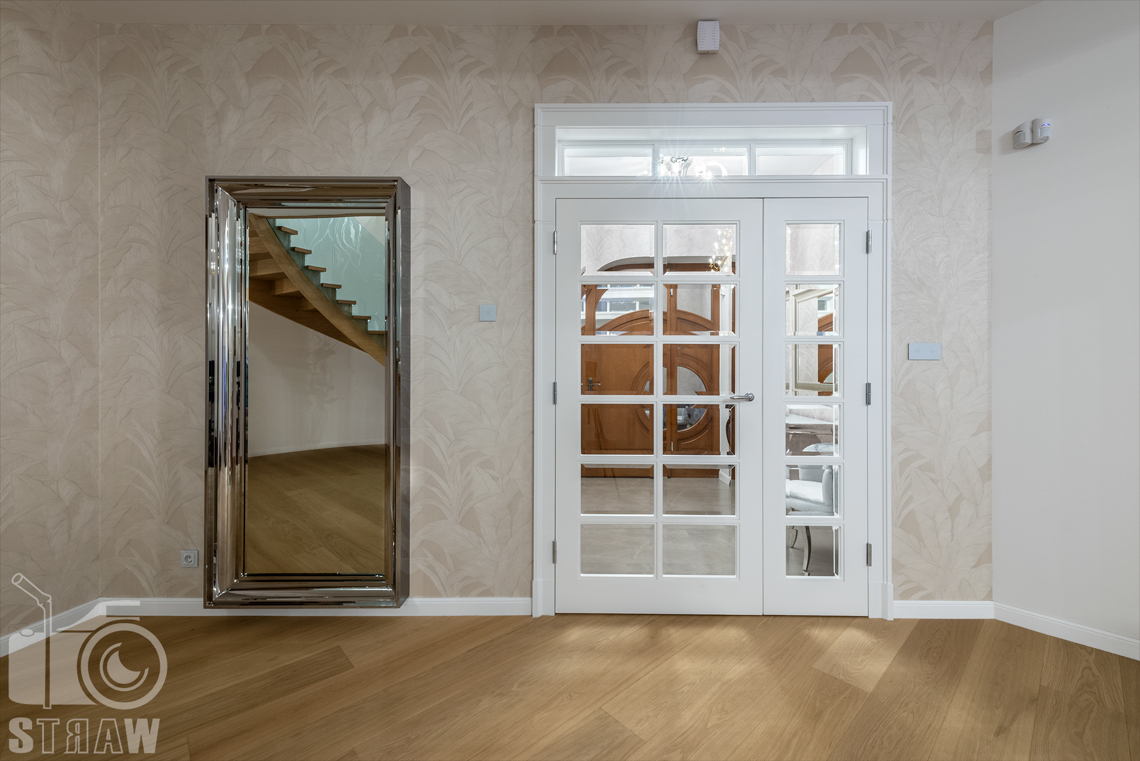 Fotografia wnętrz domu zaprojektowanego przez biuro projektowe, hol, przeszklone drzwi do przedpokoju i lustro.