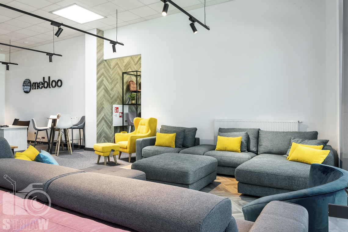 Fotografia wnętrz komercyjnych, zdjęcia showroomu meblowego Mebloo w Łodzi, na zdjęciu sofa narożnik w kolorze zieleni morskiej oraz żółty fotel.